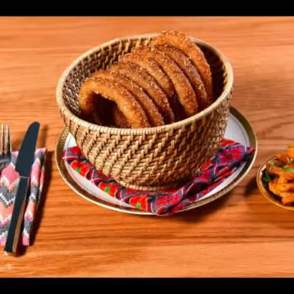 A woven basket filled with golden, ring-shaped Nepali Sel Roti, on a wooden table.