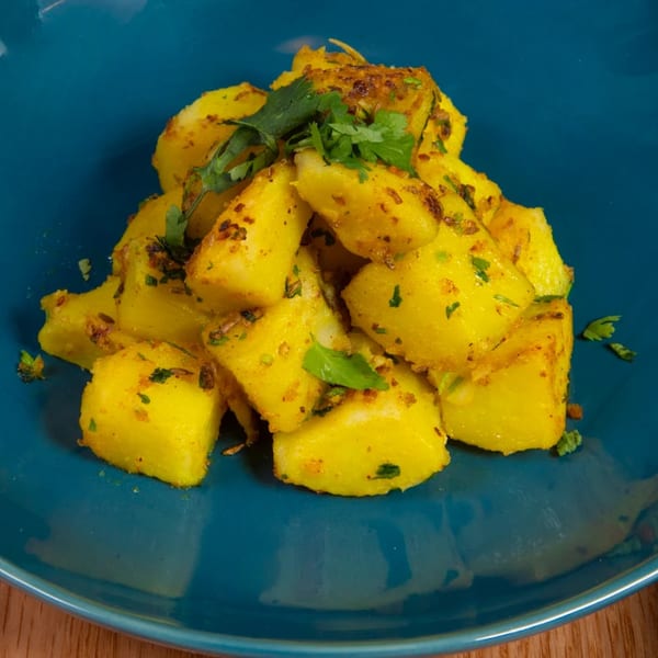 A vibrant blue plate holds a mound of golden Nepalese potato curry, garnished with fresh cilantro.