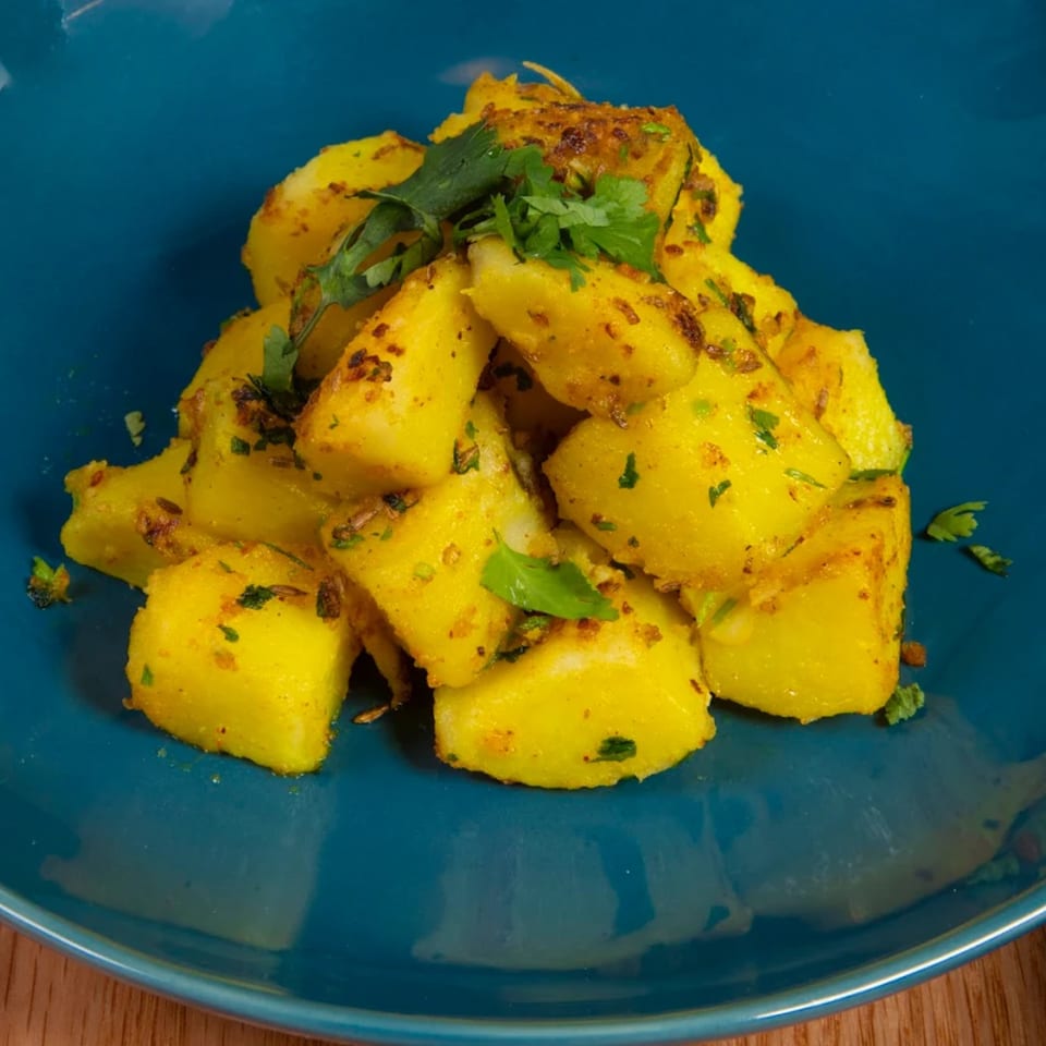 A vibrant blue plate holds a mound of golden Nepalese potato curry, garnished with fresh cilantro.