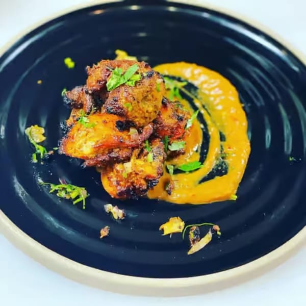Himalayan Wild Yak's chicken tikka, garnished with herbs and a swirl of orange sauce.