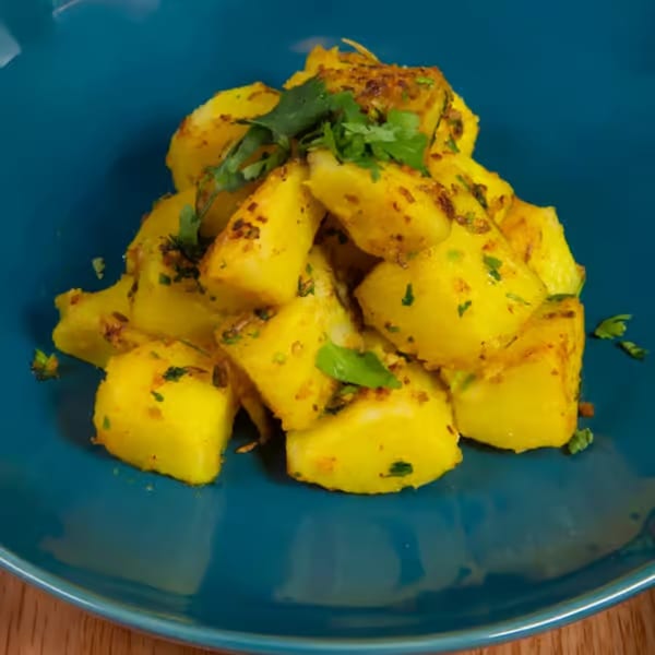 Close-up of Nepalese Aloo ko Achar, spiced potato salad, garnished with fresh cilantro on a blue plate.