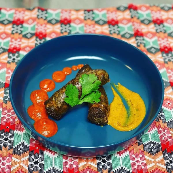 Two dark brown sausages with cilantro, red sauce, and yellow sauce on a blue plate.