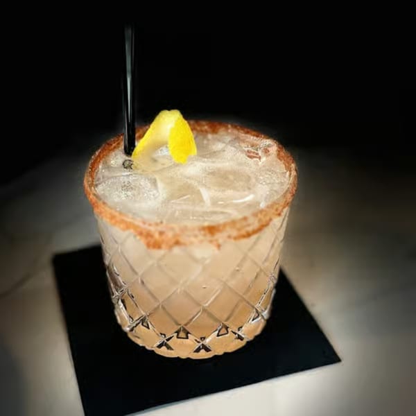 A cocktail with ice, a lemon twist, and a spiced rim, served in a textured glass.