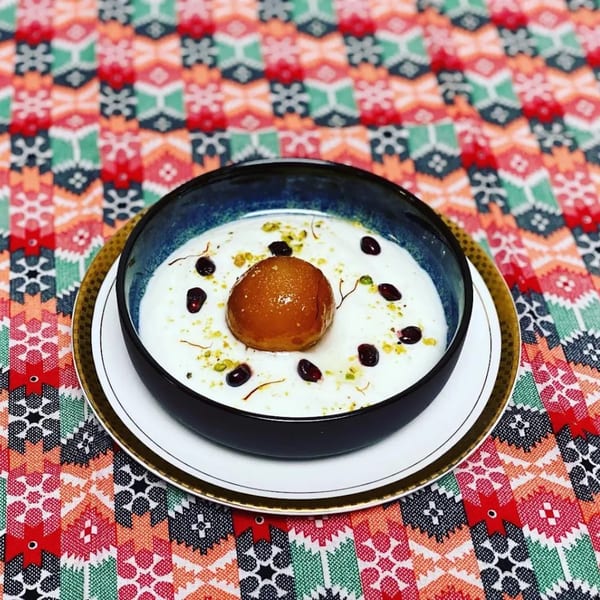 Gulab Jamun dessert in a dark bowl with white sauce, garnished with berries and saffron threads.