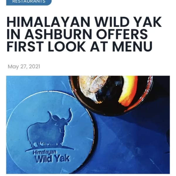 A blue coaster with a yak logo next to a dark drink with ice and a citrus slice.