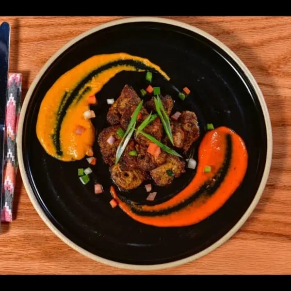 Nepalese dish with seasoned meat, orange and yellow sauces, and chopped vegetables on a black plate.