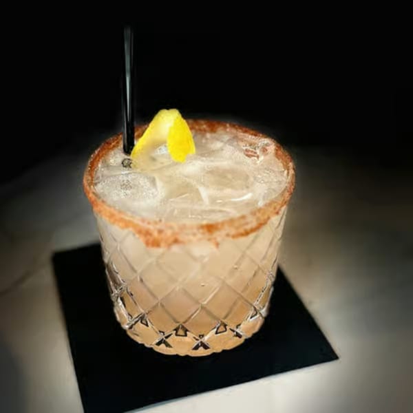 A cocktail with ice, a lemon twist, and a spiced rim in a textured glass.