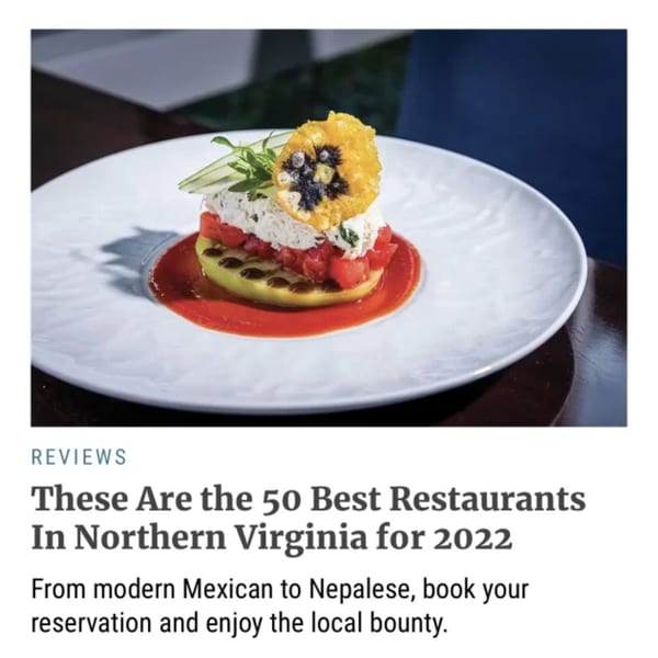 A Nepalese dish with white cheese, diced tomatoes, and a yellow edible flower on a white plate.