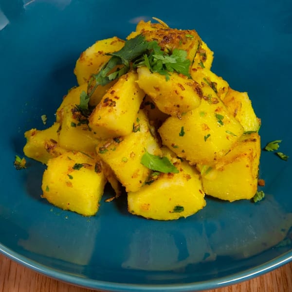Close-up of golden fried potatoes with spices and fresh cilantro on a blue plate.